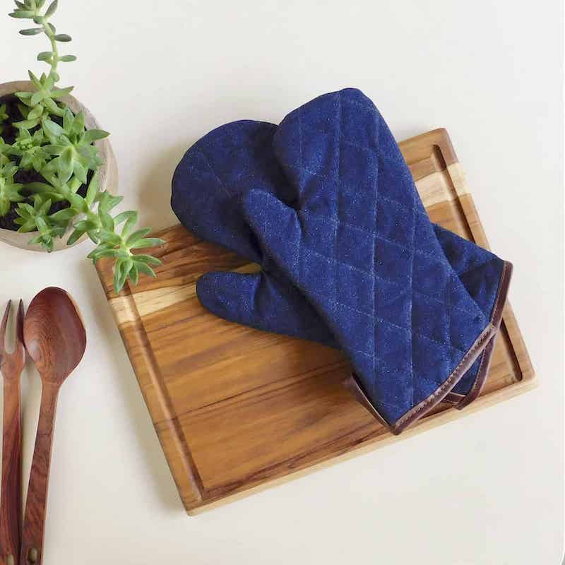 2 guantes de cocina de denim y cuero sobre una tabla de cortar de madera