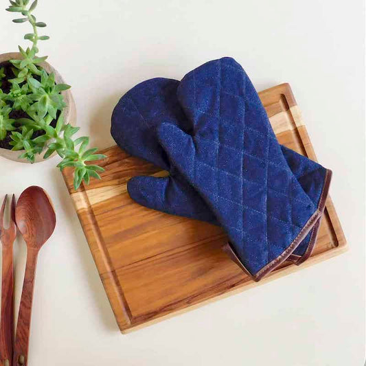 2 guantes de cocina de denim y cuero sobre una tabla de cortar de madera