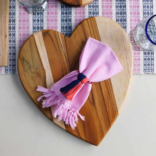 tabla en forma de corazón con una servilleta rosa encima 