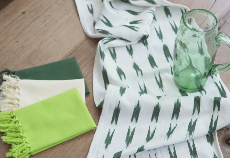 camino de mesa blanco con franjas verdes con una jarra de vidrio verde y servilletas en varios tonos de verde