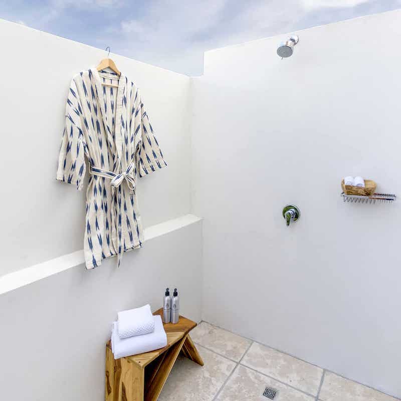 bata blanca con franjas indigo colgada en pared de ducha 